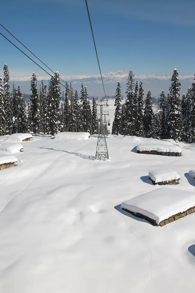 View down the Gulmarg gondola cable over snow-buried huts
